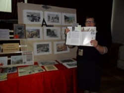 фото на котором изображена заведующая Полдневской библиотекой-сектором №19 Закшевская Ирина Алексеевна рядом с выставкой книг и фото об Афганистане, она держит в руках книгу по которой расказывает