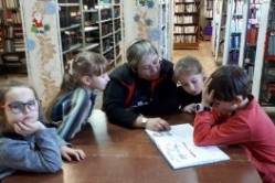 Дети с заведующей библиотекой читают книгу